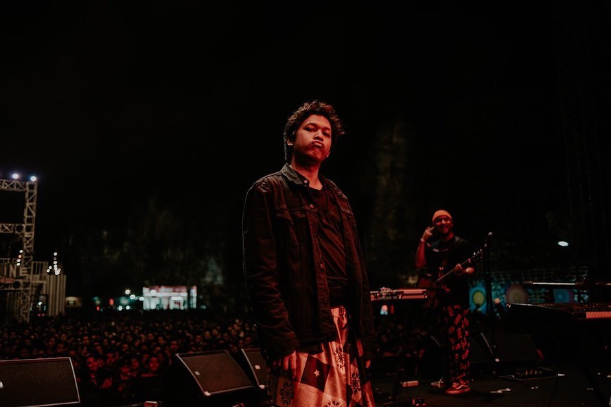 Baskara Putra atau Hindia mengenakan pakaian serba hitam ada di atas panggung